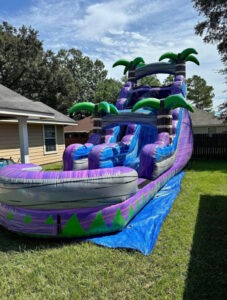 Purple and green tropical water slide with splash pool set up in a sunny Acadiana backyard for kids party games