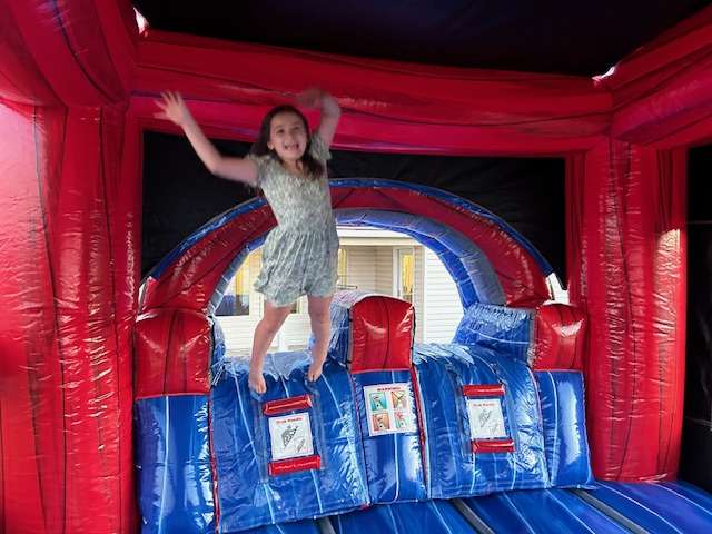 Child on a red and blue bounce house with slide at a birthday party rental