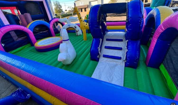 Inflatable toddler playland with soft animal figures and a small slide set up on grass at an Acadiana event