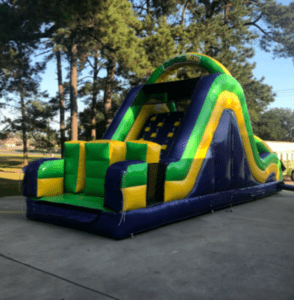 Green and purple inflatable obstacle course with a rock-climb slide set up on a paved church parking lot in Acadiana for a trunk-or-treat event