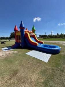 Red and blue bounce house and water slide combo with a splash pool set up on a subdivision lot in Acadiana, Louisiana, with a neighborhood street behind it
