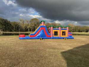 Long red, blue and orange inflatable obstacle course set up on an open field in Acadiana, Louisiana — a rental unit teens and adults can race through