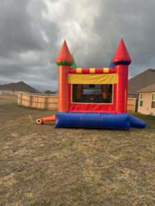 Red, blue and yellow castle bounce house set up on a real backyard lawn in Acadiana, showing a residential grassy yard used for a Patriot Jumps rental