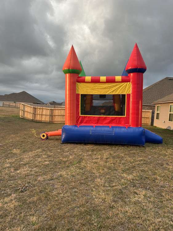 Red, blue and yellow castle bounce house set up on a real backyard lawn in Acadiana, showing a residential grassy yard used for a Patriot Jumps rental