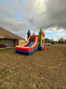 Red, blue, and yellow marble castle combo bounce house with an attached slide set up on a grassy Acadiana yard, ideal for a school fundraiser fun day