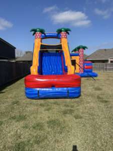 Red and orange tropical castle bounce house and water slide combo set up in a sunny fenced backyard in Acadiana