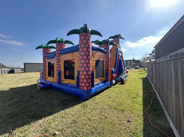 Tropical bounce house and slide combo set up along a wooden privacy fence in a Lafayette area subdivision backyard