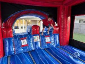 Boy playing on the inflatable obstacle bumps inside a red and blue Patriot Jumps bounce house, showing the interior play surface and safety placards