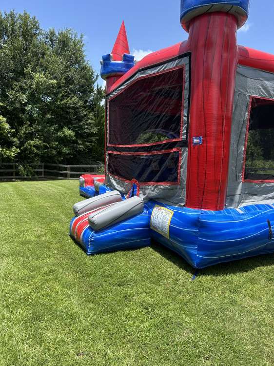 Red and blue marble castle bounce house set up on a flat, level green grass lawn beside a home in Acadiana, an ideal surface for a safe bounce house rental