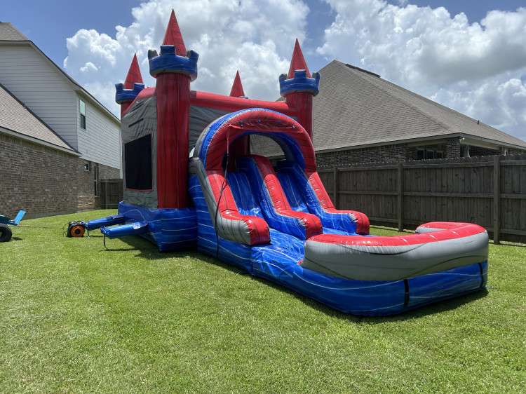 Red and blue bounce house and slide combo rental set up on green grass in an Acadiana backyard for a fall birthday party