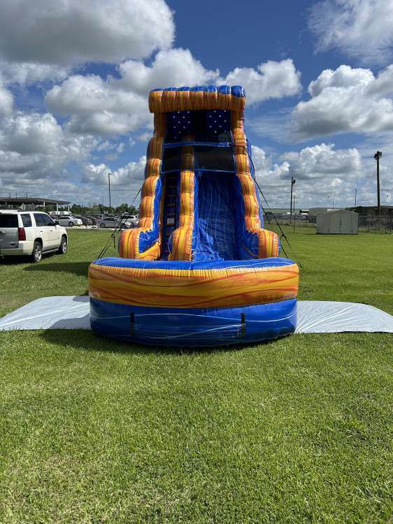 Tall blue and orange marble water slide rental in an open Acadiana field for an early-fall birthday party