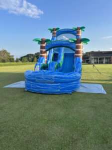 Blue tropical palm tree water slide rental with splash pool set up on a green lawn in Acadiana, Louisiana
