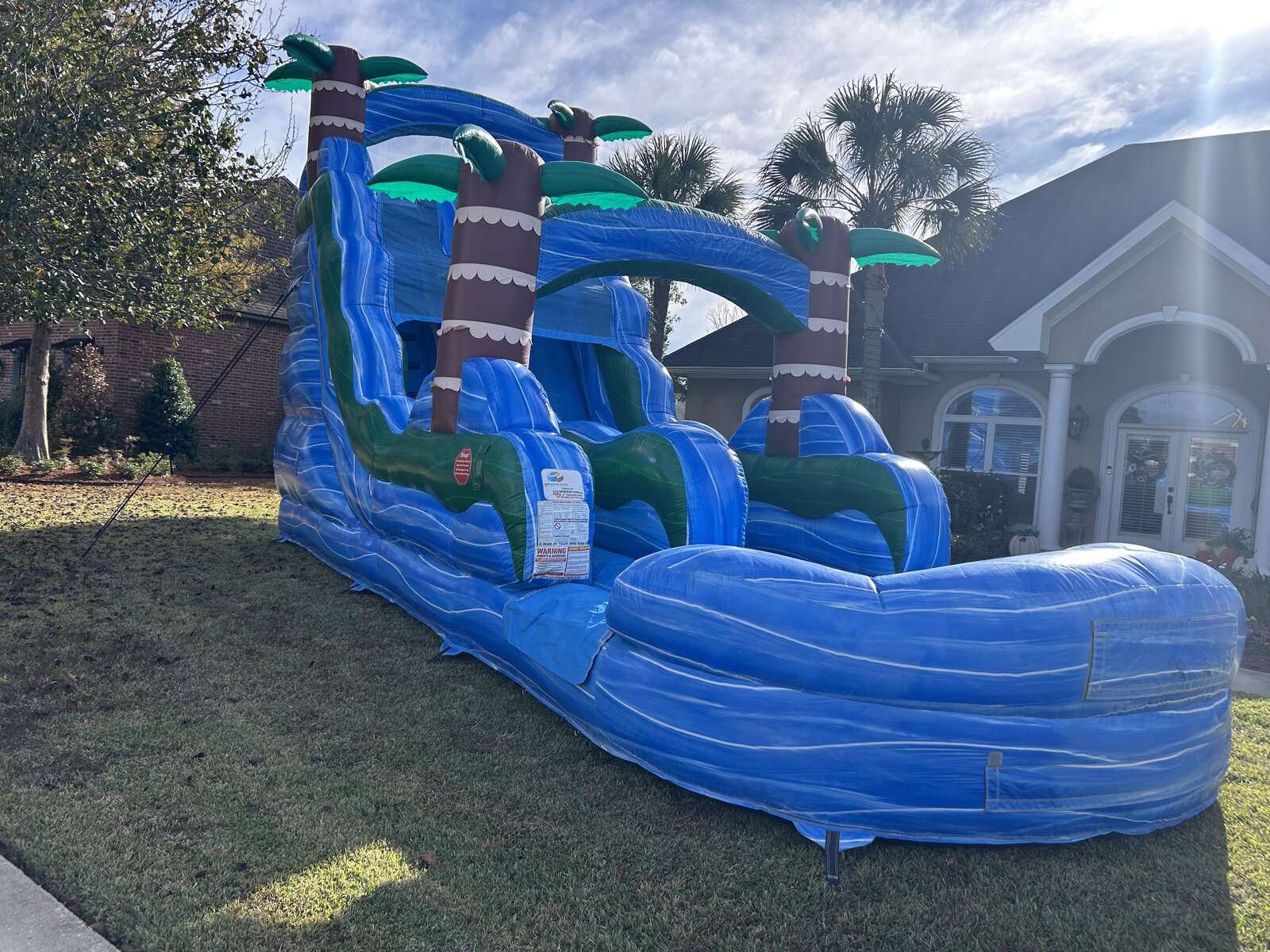 Blue tropical palm-tree inflatable water slide with splash pool anchored in a front yard in Youngsville, Louisiana