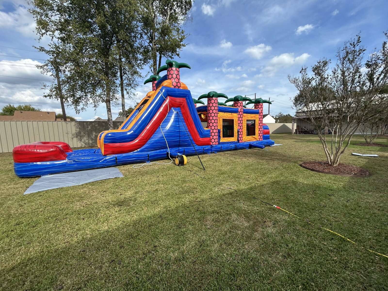 Large tropical red, blue and orange obstacle course with attached slide set up on grass for a neighborhood block party in Youngsville, Louisiana