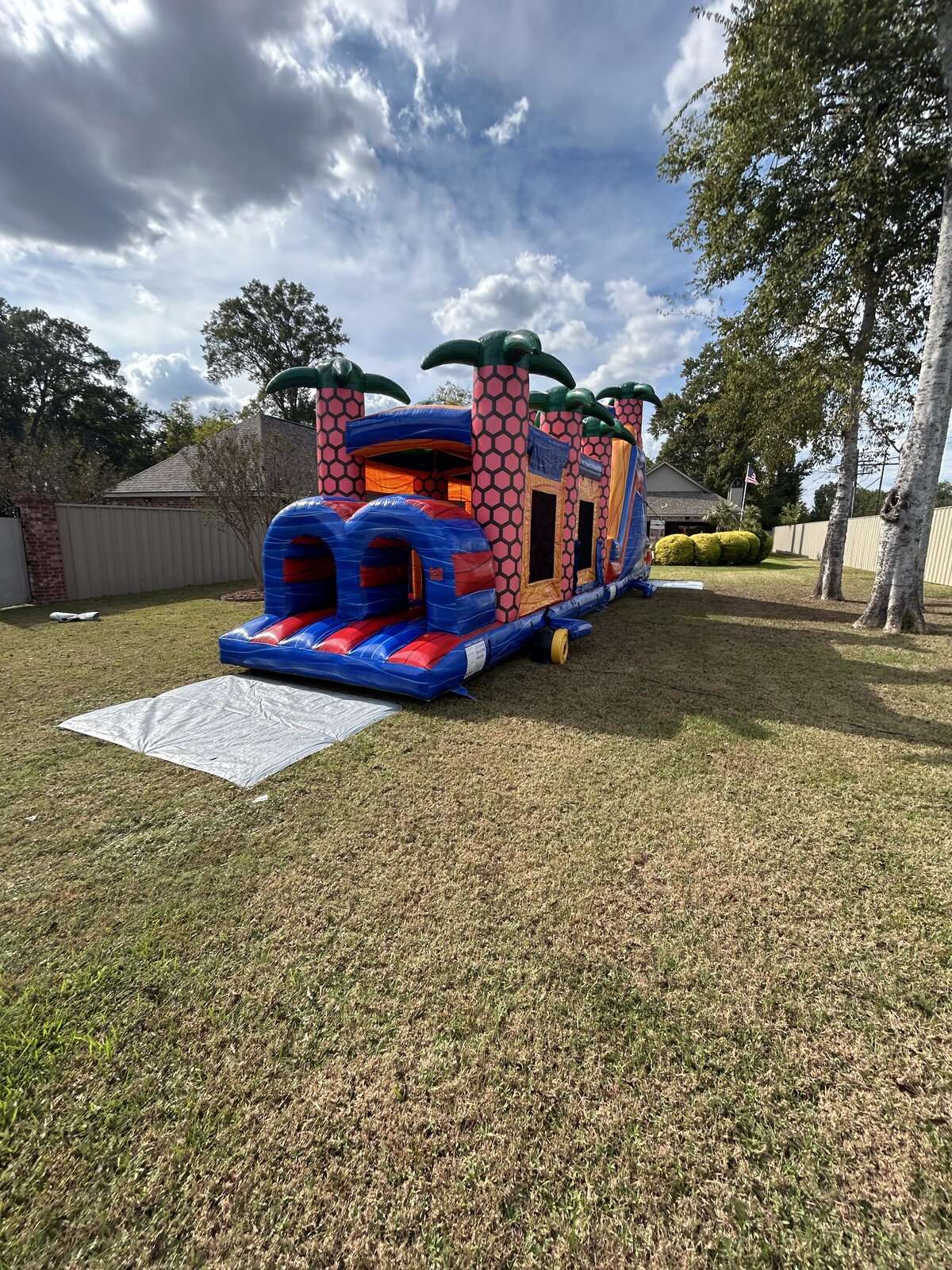 Red and blue bounce house and slide combo set up in a shaded backyard for a hot Louisiana summer day