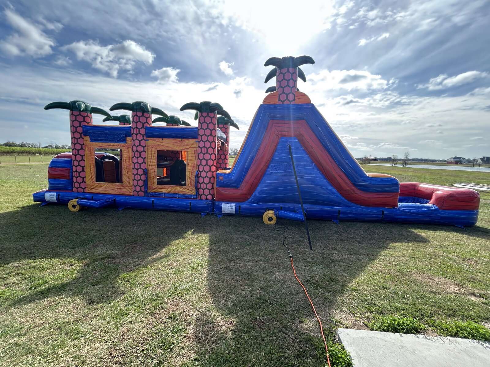 Red, blue, and orange tropical obstacle course and slide combo set up in a wide open field for a park event in Acadiana