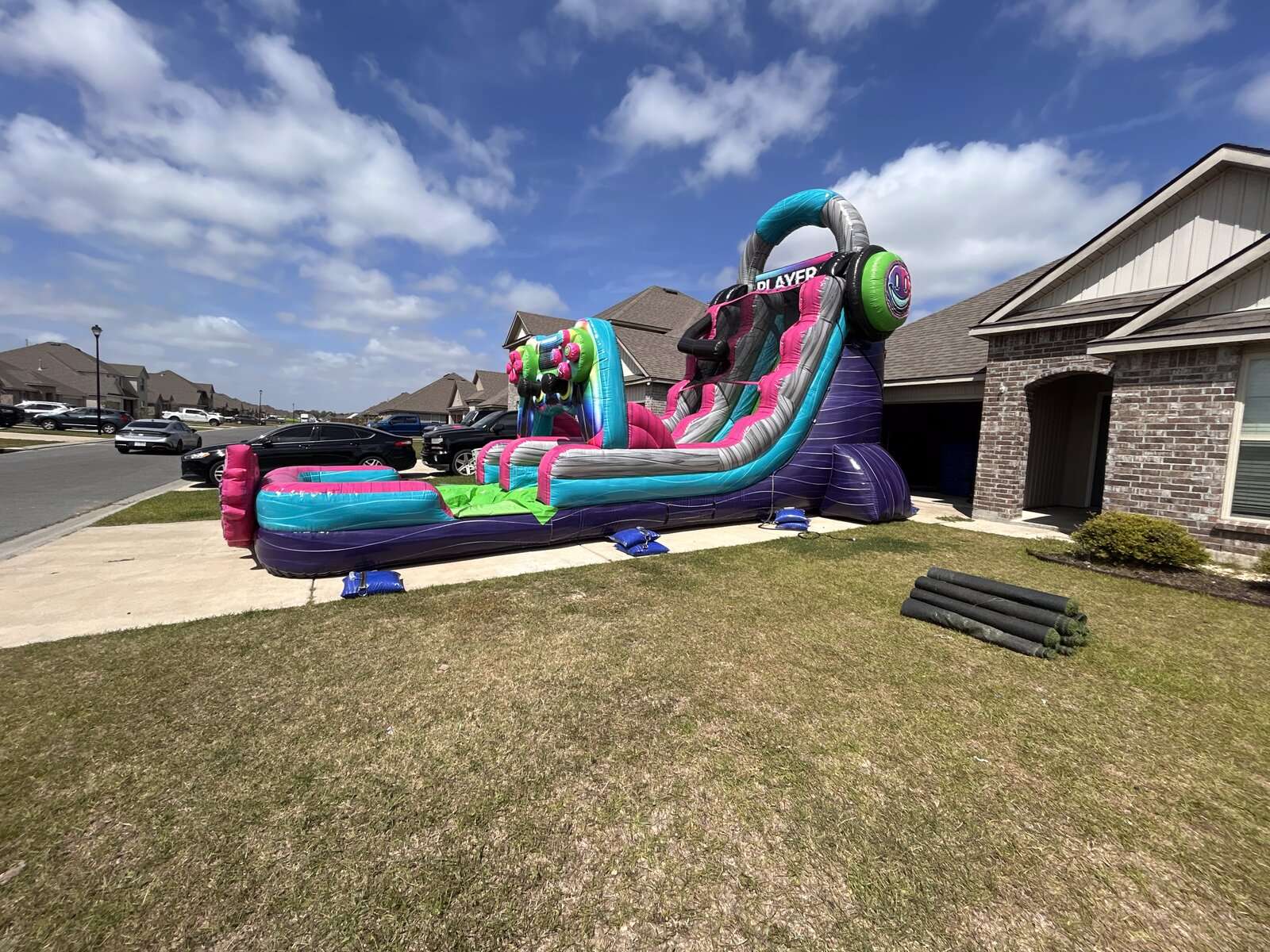 Glitch-themed inflatable water slide set up on a hard-surface driveway in a Youngsville, LA subdivision, anchored with sandbags