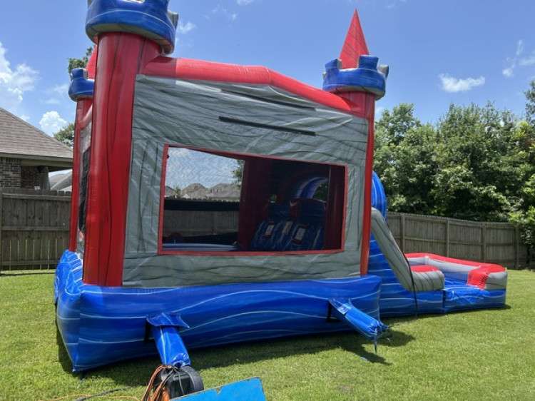 Red and blue castle combo bounce house with slide set up on a sunny fenced lawn as a wedding reception kids’ zone in Acadiana