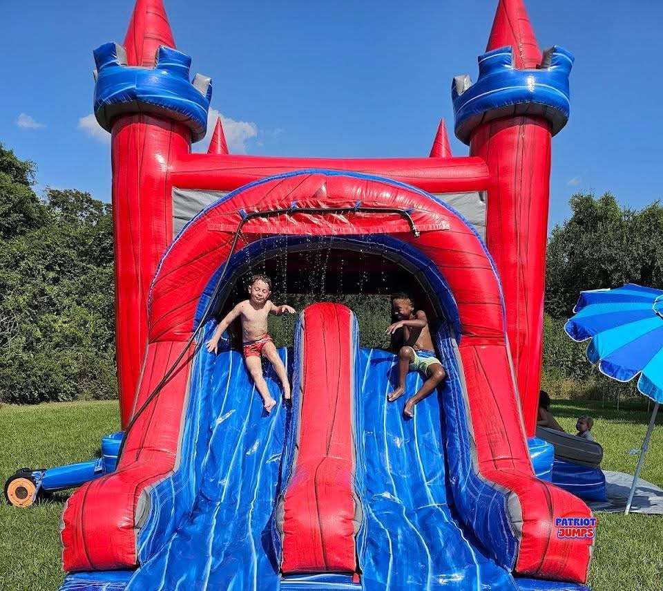 Two kids sliding down a clean, freshly sanitized red and blue water slide bounce house rental in Acadiana