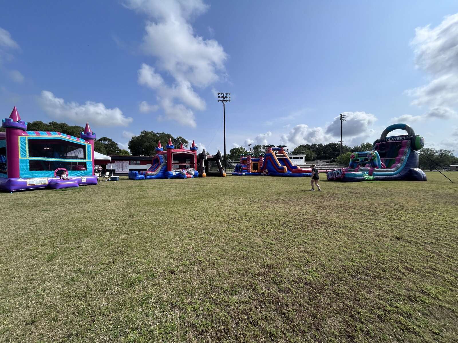 Multiple bounce houses, water slides and an obstacle course set up in a row on an open ball field for a large corporate event in Lafayette, LA