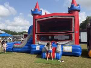 Red and blue castle combo bounce house rental set up on a grass field at an end-of-summer community party in Acadiana with families and kids