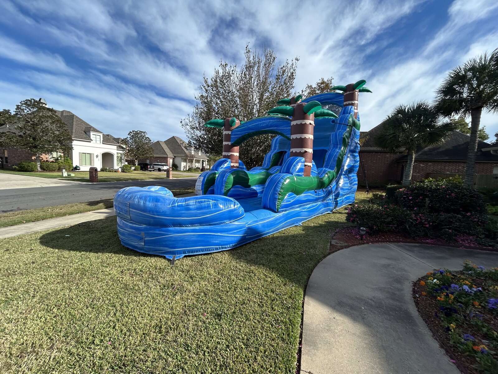 Blue tropical palm-tree water slide rental with splash pool in a front yard in Youngsville, Louisiana for an end-of-summer party