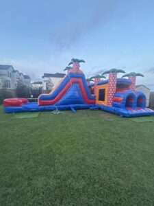 Tropical obstacle course and slide bounce house rental set up on grass at twilight for an evening party in Acadiana