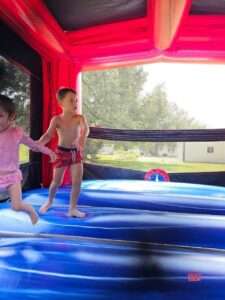 Kids jumping inside a red and blue bounce house rental in an Acadiana backyard