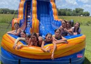 A group of about ten happy kids cooling off in the splash pool of a Patriot Jumps water slide at an Acadiana party