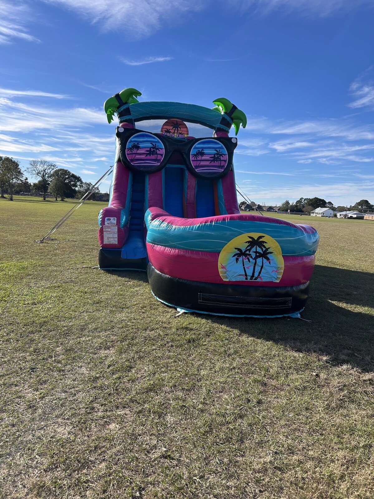 Pink and teal tropical water slide rental in an open Acadiana field, ready for an end-of-summer Labor Day party