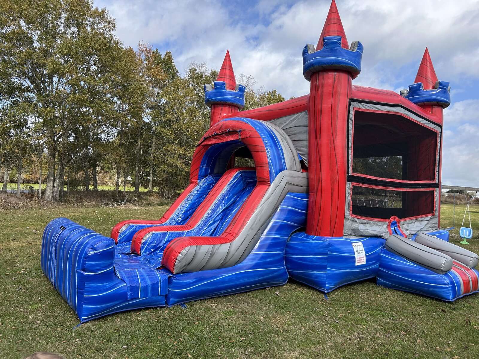 Red and blue castle combo bounce house with slide set up on grass for a summer camp party rental in Acadiana