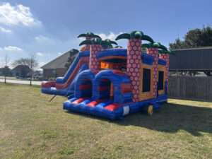 Large red, blue and purple inflatable bounce house and slide combo set up in an open field for a grand opening event in Acadiana