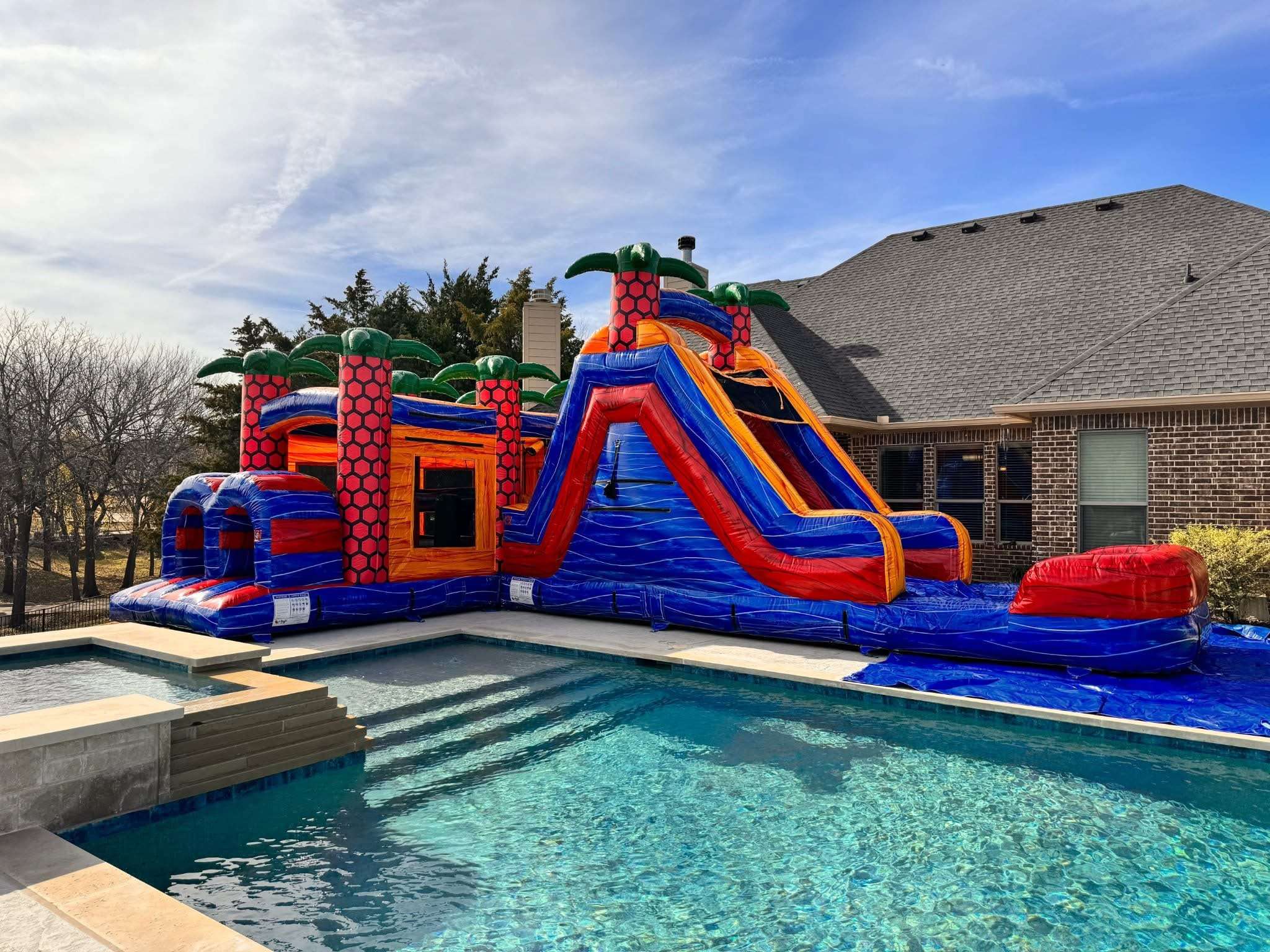 Large water slide combo rental anchored with sandbags on a hard patio surface beside a backyard pool in Acadiana