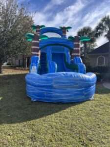 Blue tropical palm tree water slide rental with splash pool set up in the front yard of a Lafayette, LA home