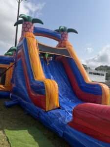 Tall tropical marble inflatable water slide rental set up on an open field with a child at the top platform in Lafayette, Louisiana