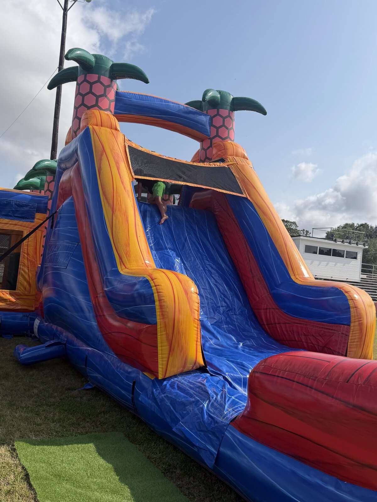 Tall tropical marble inflatable water slide rental set up on an open field with a child at the top platform in Lafayette, Louisiana
