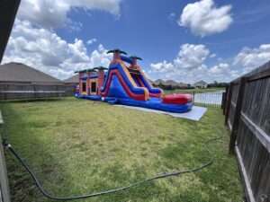 Red and blue bounce house and water slide combo rental set up in a fenced Broussard, LA backyard with a splash pool