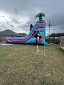 Tropical water slide combo rental staked and strapped down on a level backyard lawn in Lafayette, LA, with anchor straps running to ground stakes