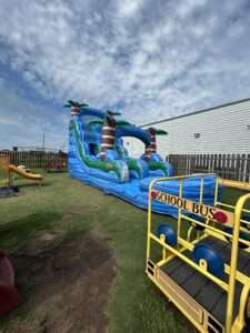 Tall blue and green tropical water slide rental with a splash pool set up in a fenced Acadiana backyard, positioned so a supervising adult has a clear view of the slide exit
