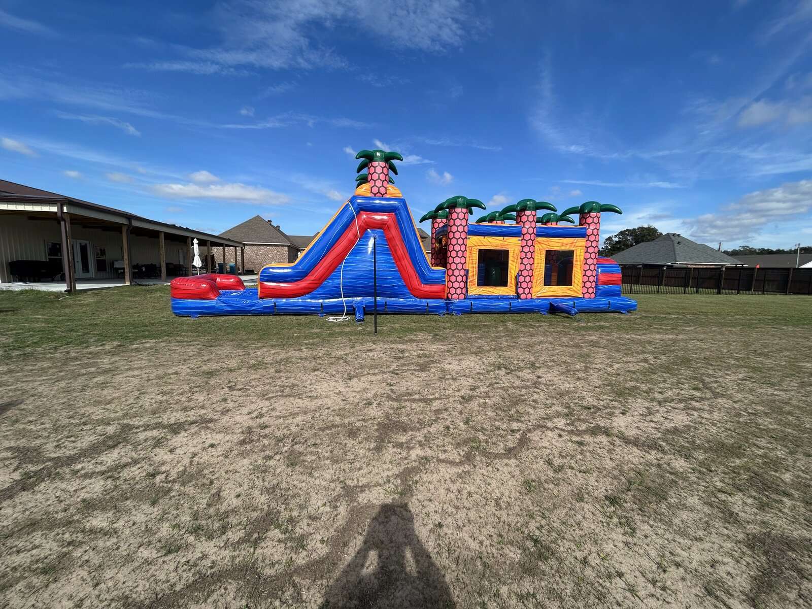 Red and blue inflatable bounce house and slide combo set up dry on green grass under a bright blue sky in Acadiana