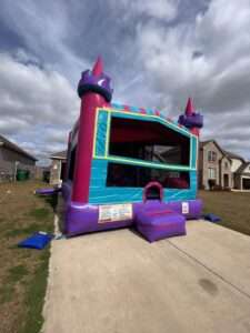Pink and purple castle bounce house rental set up on a driveway for a toddler birthday party in Acadiana