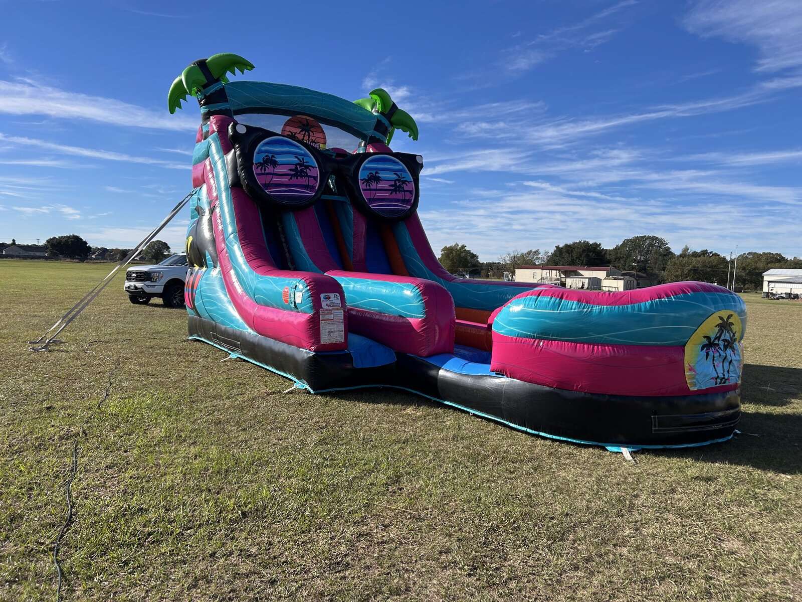 Pink and teal tropical water slide rental set up wet with a splash pool on a sunny open field in Acadiana, Louisiana