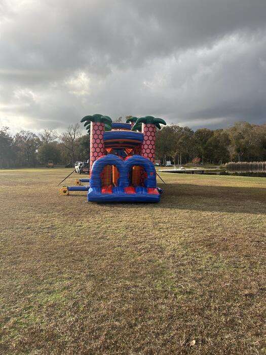 Purple and pink bounce house and slide combo rental standing alone in an open Acadiana field under heavy dark storm clouds, the kind of sky that knocks out power mid-party