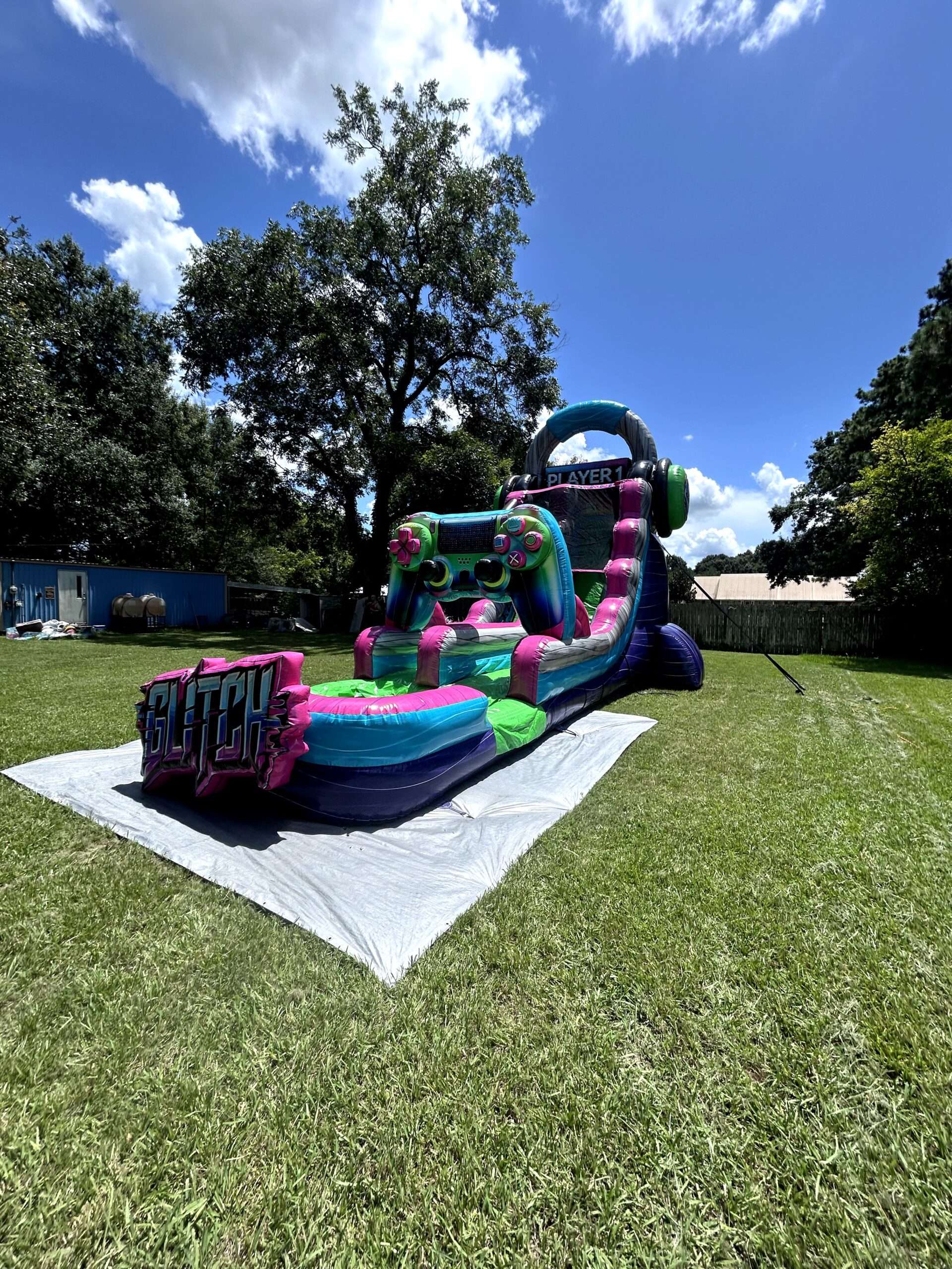 A teal and pink inflatable water slide sitting on a white protective tarp laid over backyard grass, showing how the ground is covered before setup.