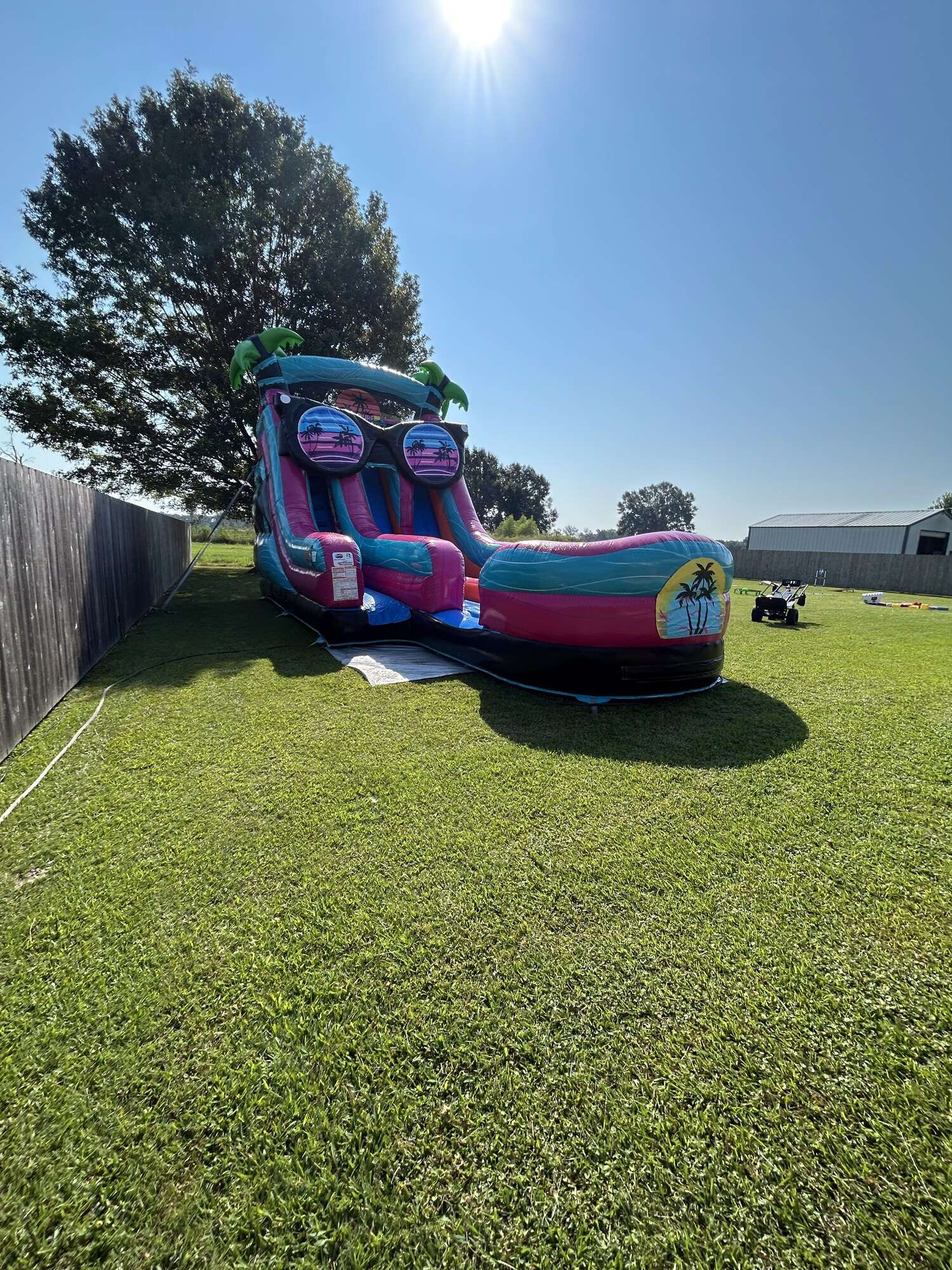 Pink and teal water slide rental set up and inflated in a fenced Youngsville, LA backyard on the morning of a booked party