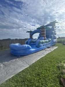 Tall blue inflatable slide set up on a tarp in a backyard under a cloudy sky in Lafayette, LA