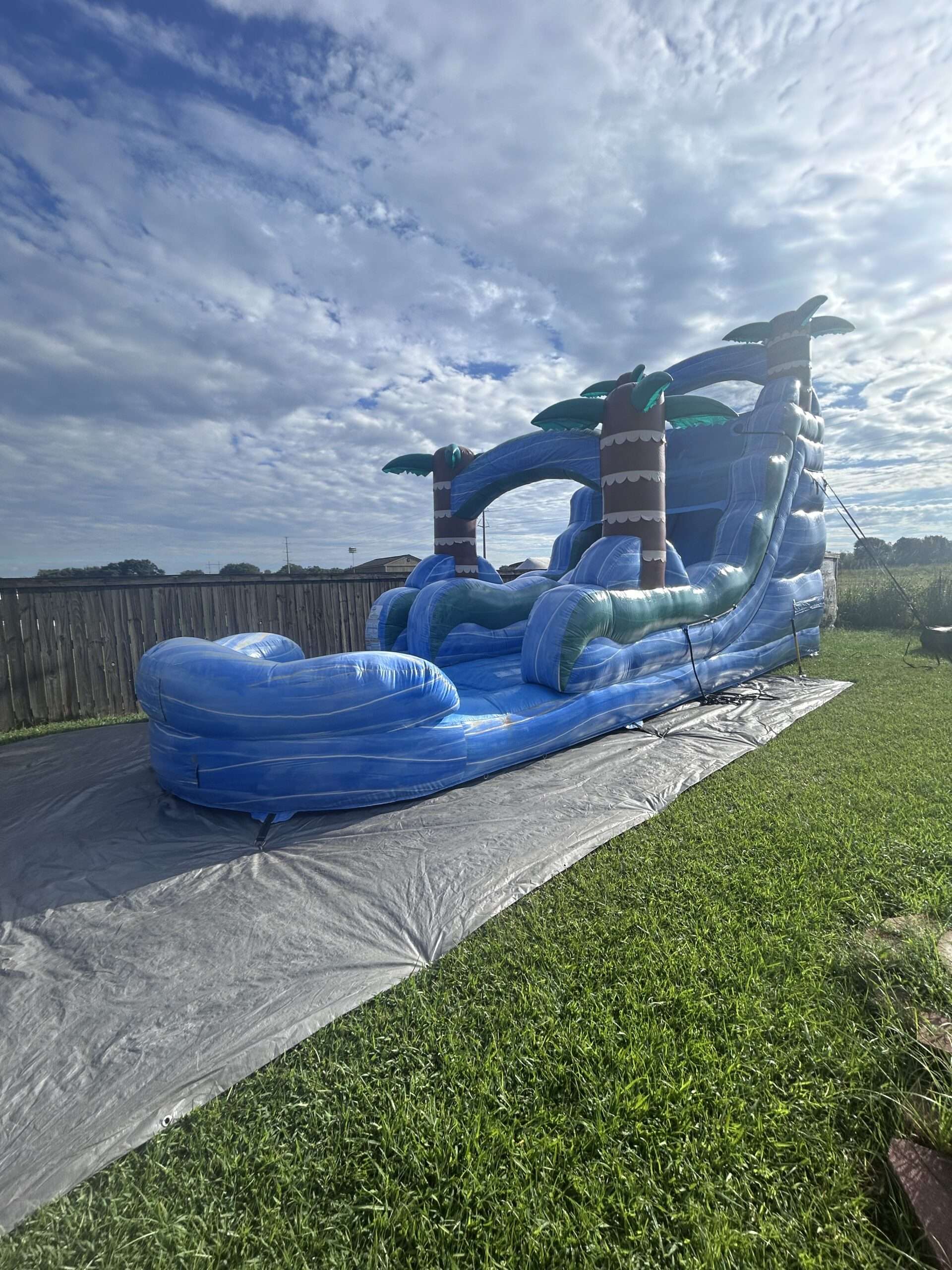 Tall blue inflatable slide set up on a tarp in a backyard under a cloudy sky in Lafayette, LA