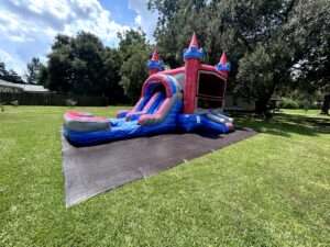 A red and blue castle bounce house combo with an attached splash pool set up on a wide, freshly mowed green lawn in Acadiana.
