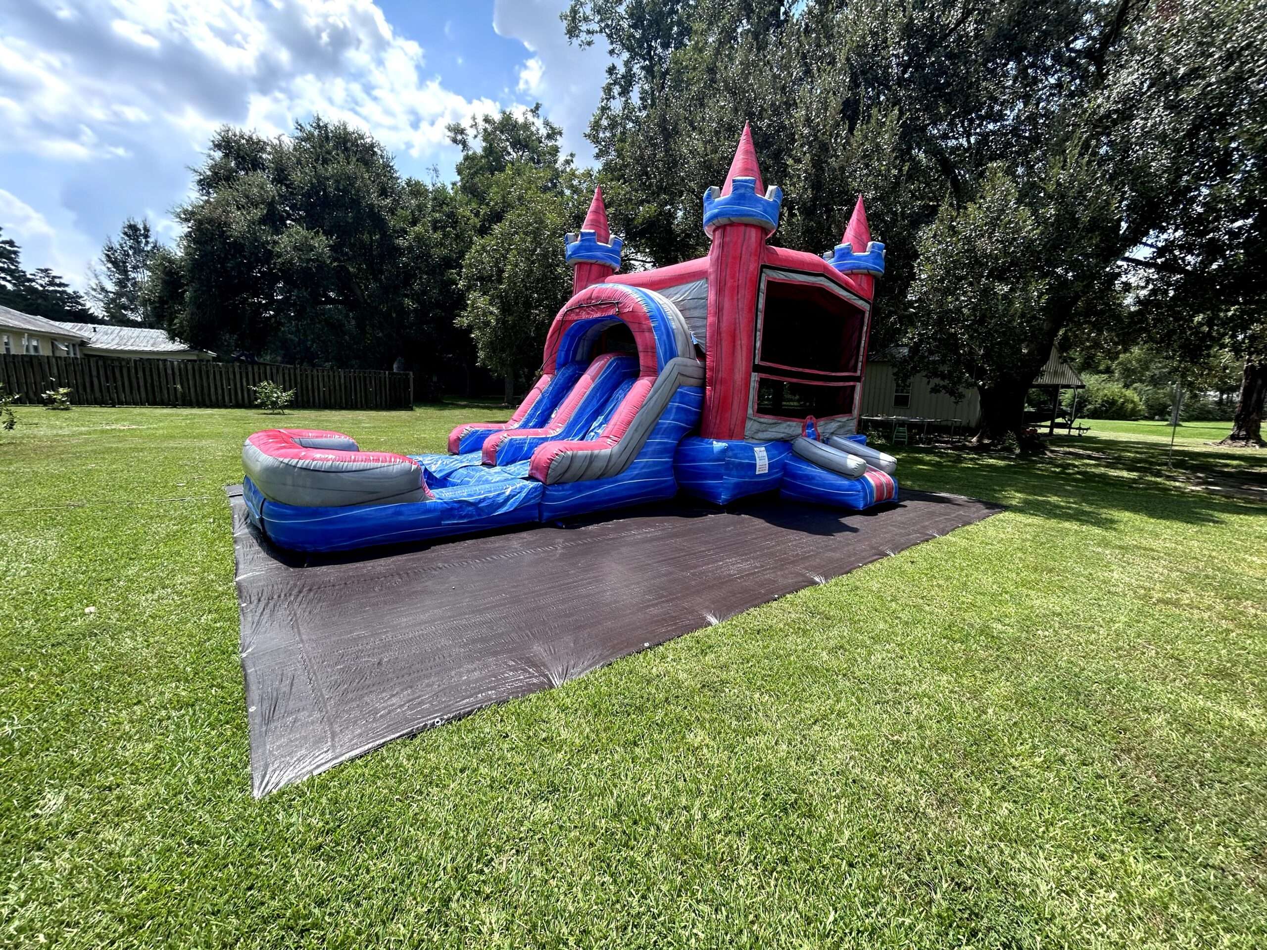 A red and blue castle bounce house combo with an attached splash pool set up on a wide, freshly mowed green lawn in Acadiana.