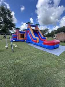 Purple and orange bounce house water slide combo with a splash pool set up on green grass in an open Acadiana yard, blower running at the back of the unit.
